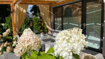 A covered outdoor seating area with a pergola, white hydrangea flowers, and a glass door leading to a patio.