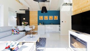 A modern living room with a grey sofa, a coffee table, and a fireplace. There is a kitchen area with white cabinets and a blue accent wall.