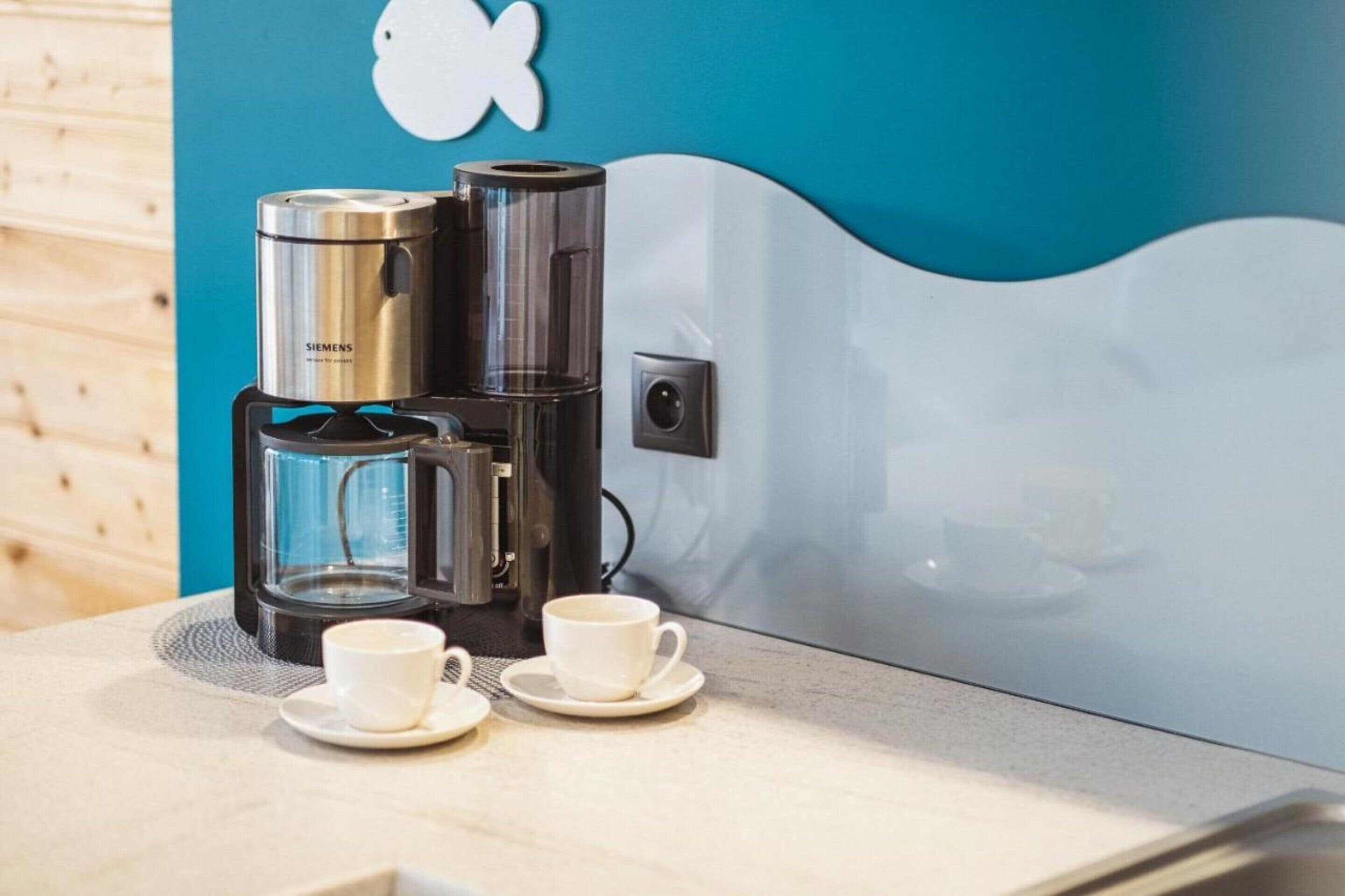 A coffee maker with two cups on a table.