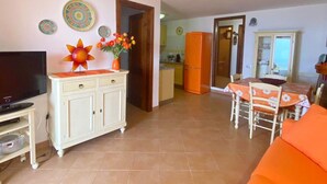 Una sala de estar con televisor, un mueble aparador y un comedor con mesa y sillas.