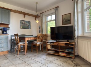 A dining area with a wooden table, chairs, a television, and a bookshelf.