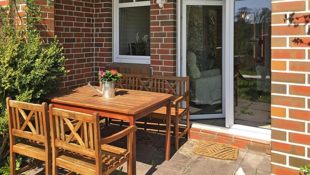 A patio with a wooden table and chairs, a potted plant, and a sliding glass door. - Ferienwohnung, Fedderwardersiel (Butjadingen)
