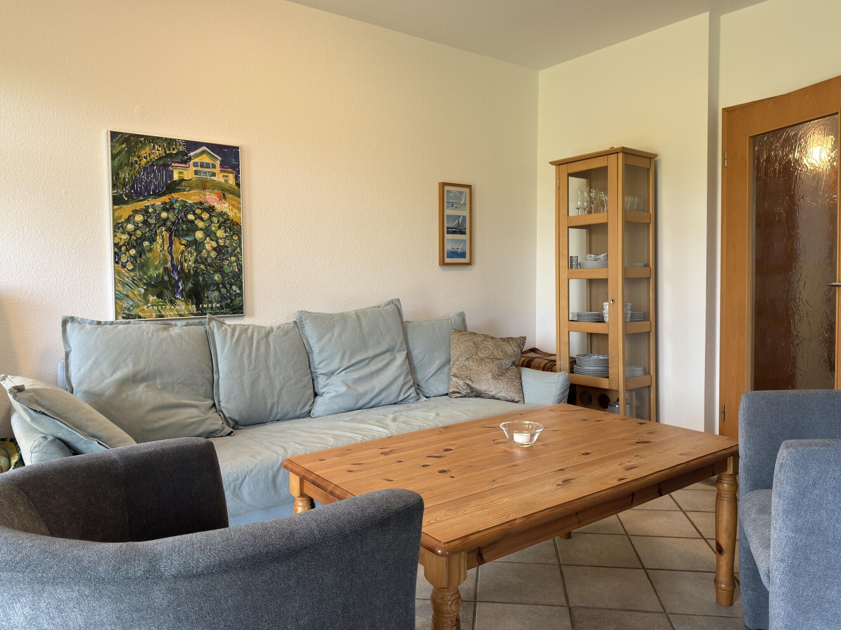 A living room with a sofa, two armchairs, a wooden coffee table, a glass cabinet, and a painting on the wall.