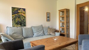 A living room with a sofa, two armchairs, a wooden coffee table, a glass cabinet, and a painting on the wall. - Ferienwohnung, Fedderwardersiel (Butjadingen)