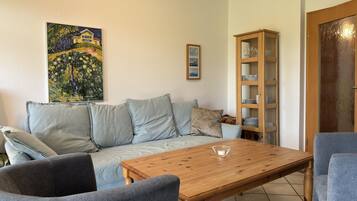 A living room with a sofa, two armchairs, a wooden coffee table, a glass cabinet, and a painting on the wall.