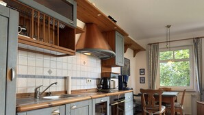 A kitchen with wooden cabinets, a sink, a stove, and a dining area with chairs. - Ferienwohnung, Fedderwardersiel (Butjadingen)
