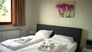 Ein Hotelzimmer mit einem ordentlich bezogenen Bett, einem Tulpenbild an der Wand und einem Laptop auf einem Nachttisch.