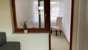Ein Zimmer mit großem Fenster, einem Blumentopf, einem grauen Sofa und einem weißen Sessel.