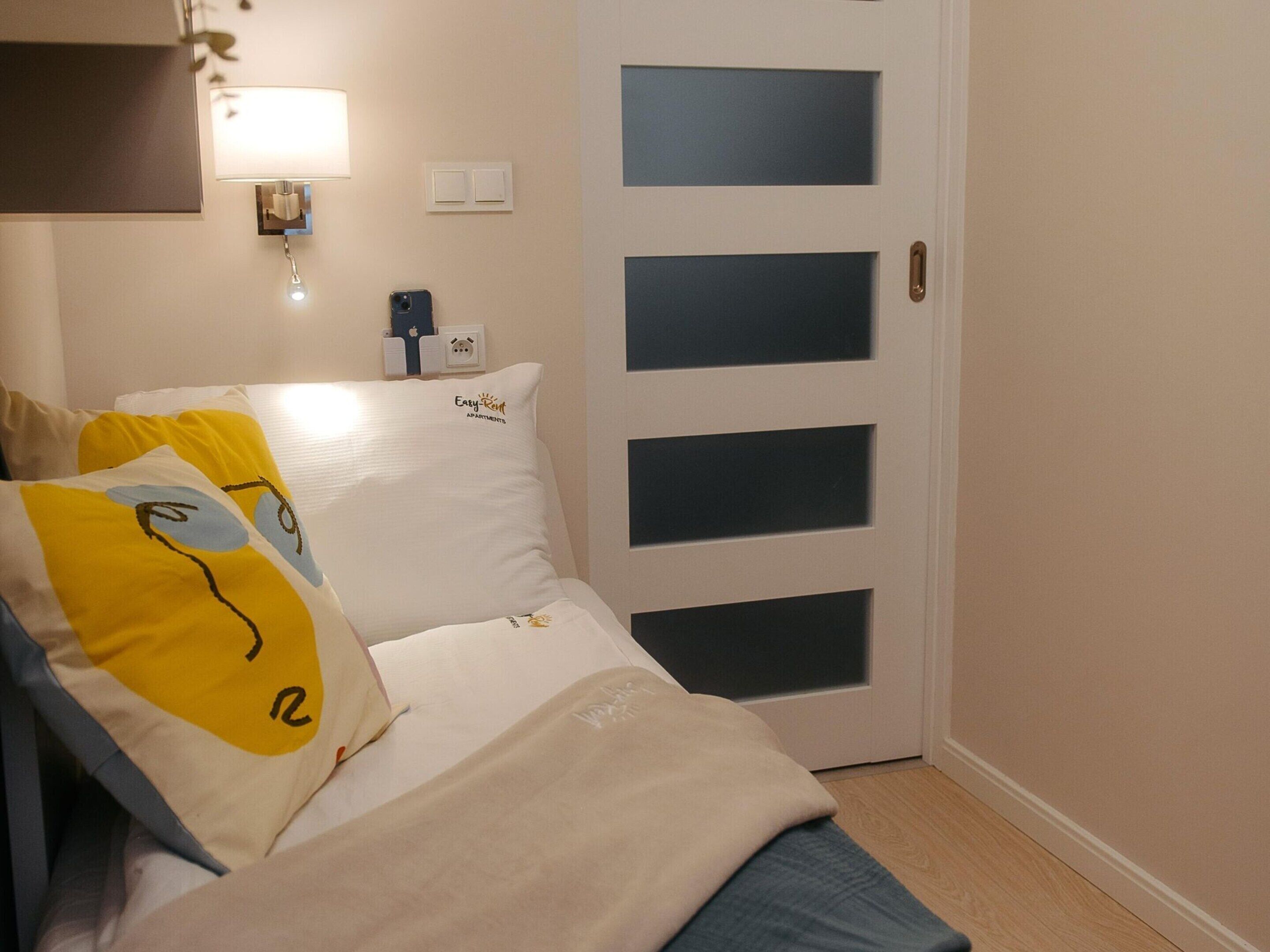 Een slaapkamer met een bed, kussens, een nachtkastje, een lamp en een deur met geëtste ruitpanelen.