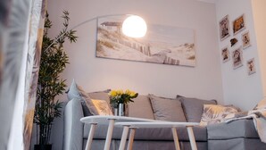 Un salon moderne avec un canapé gris, une table ronde, un lampadaire et un grand tableau représentant une scène de plage.