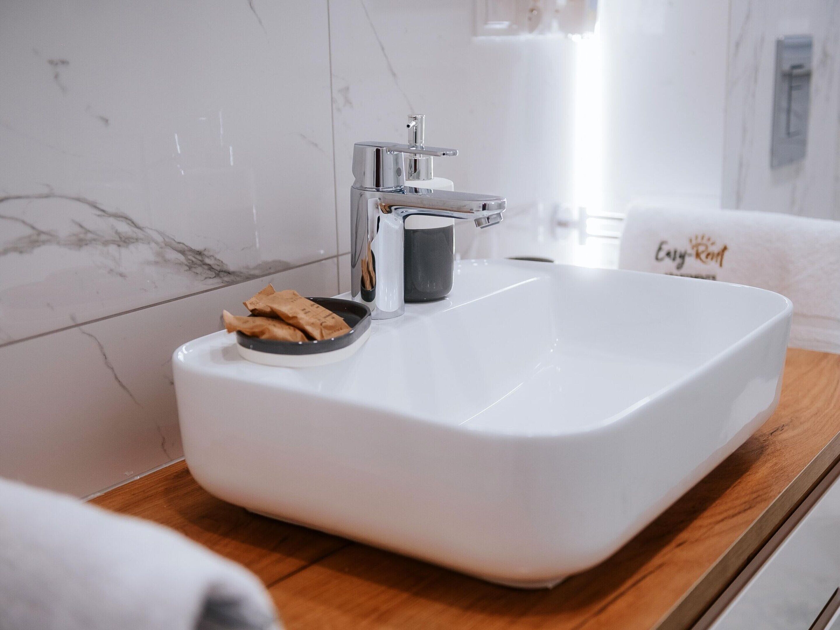 A bathroom with a white sink, a marble backsplash, and a towel with a logo.