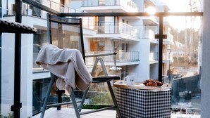 Un balcon moderne avec une chaise, un pouf à carreaux et un plateau sur lequel se trouvent un croissant et une tasse.