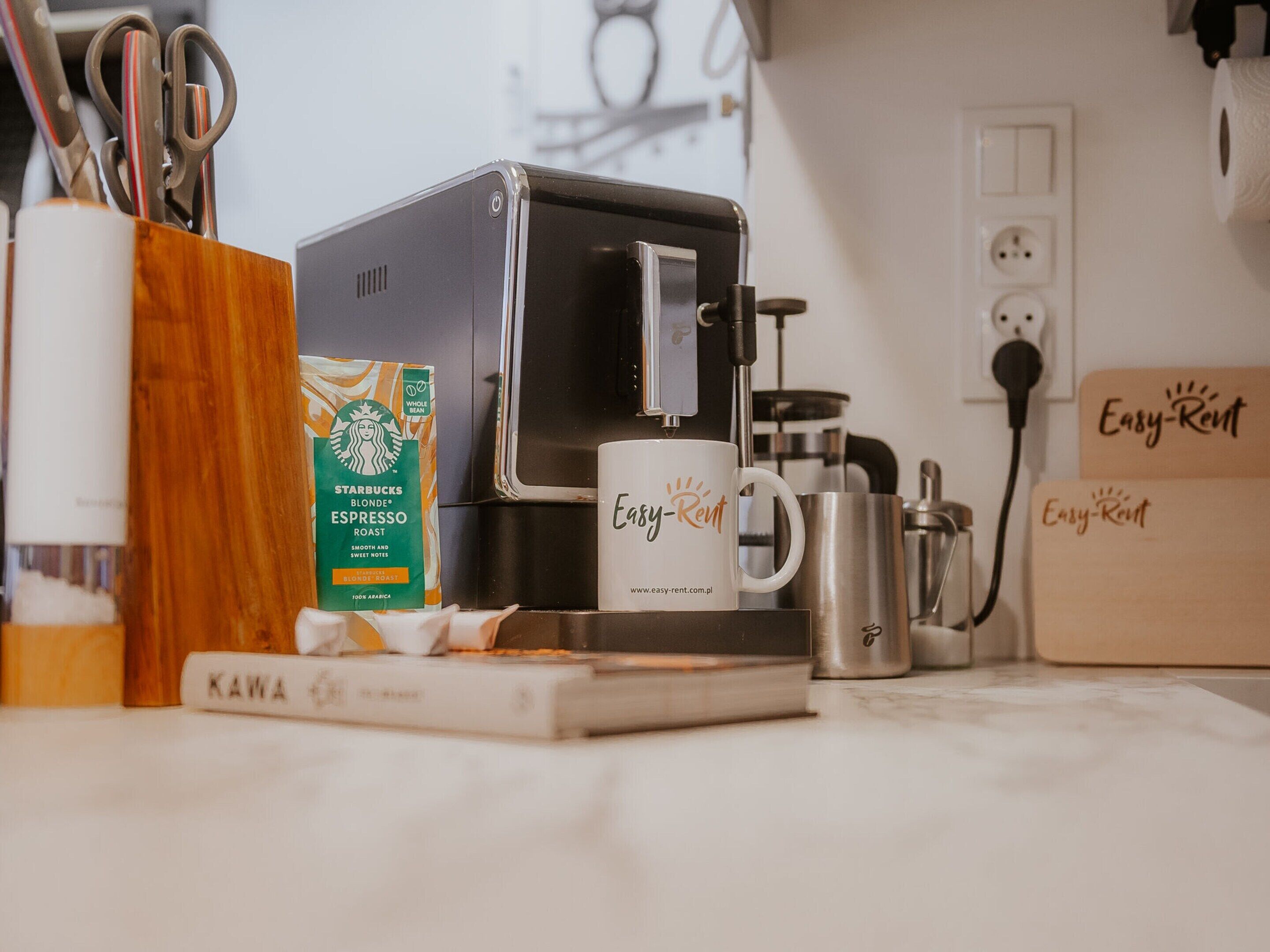 Eine Kaffeemaschine, eine Starbucks-Kaffeekapsel, eine Tasse und eine Kiste mit der Aufschrift 'Easy-Rent' auf einer Küchenarbeitsplatte.