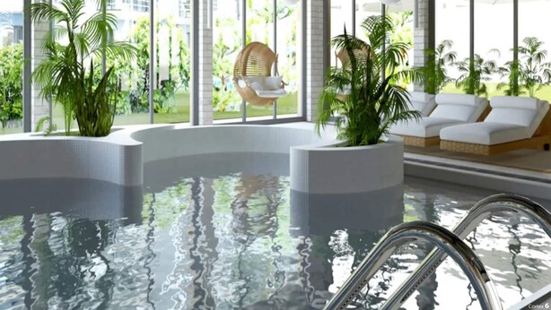 Un espace piscine intérieur moderne, offrant une vue dégagée sur l’extérieur, avec un salon doté de canapés blancs et d’un fauteuil suspendu, le tout agrémenté de plantes en pot.