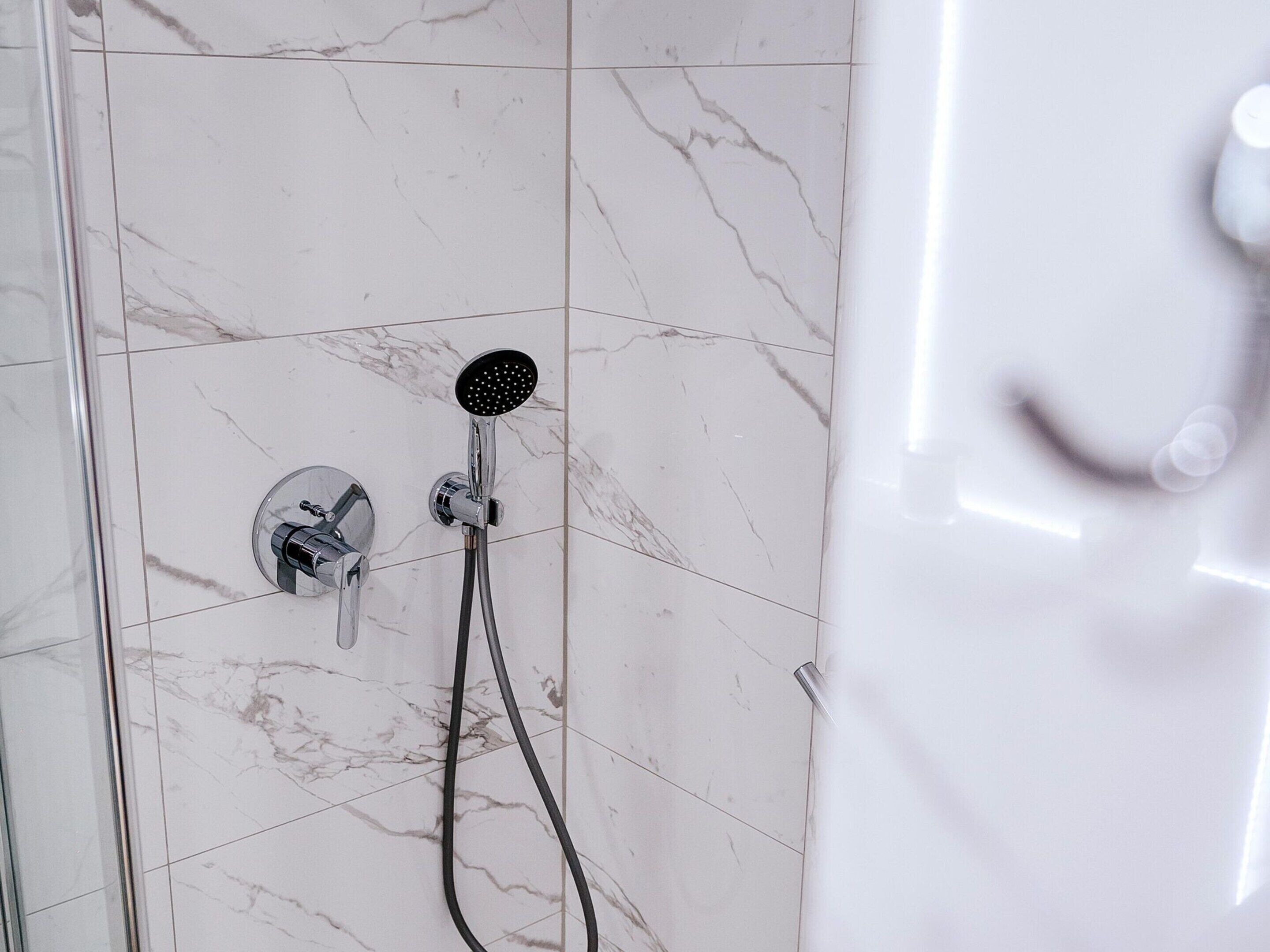 A bathroom with a shower, a glass door, and a marble floor.