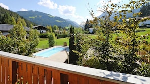 A residential area with a wooden deck overlooking a swimming pool, surrounded by lush greenery and houses. - Apartment House Isegrim, Altenmarkt (Altenmarkt im Pongau)
