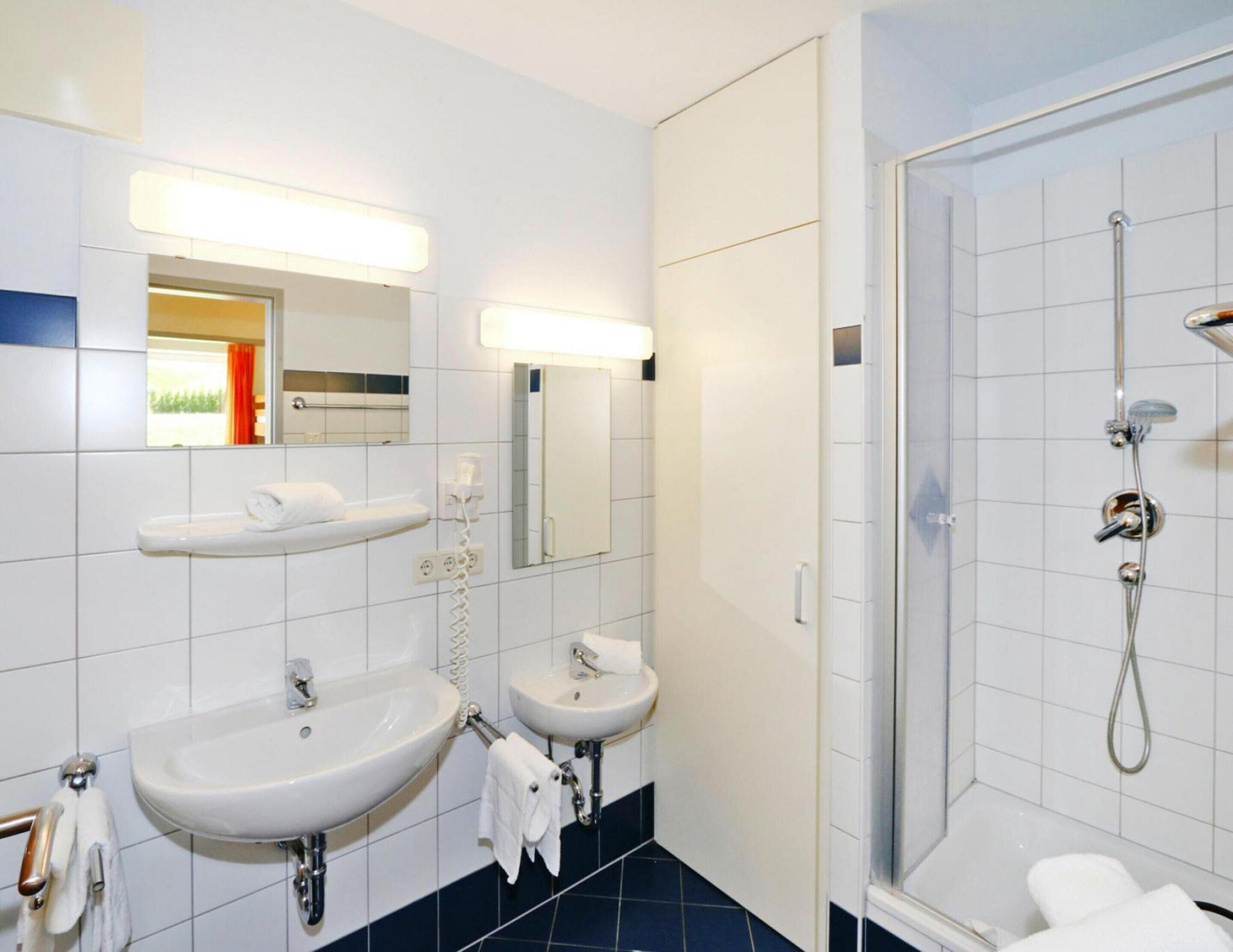 A modern bathroom with two sinks, a shower, and a mirror.