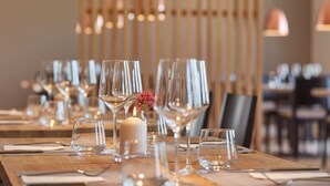Une salle de restaurant avec une longue table en bois dressée pour le dîner, agrémentée de beaux verres et d’un petit chandelier servant de centre de table.