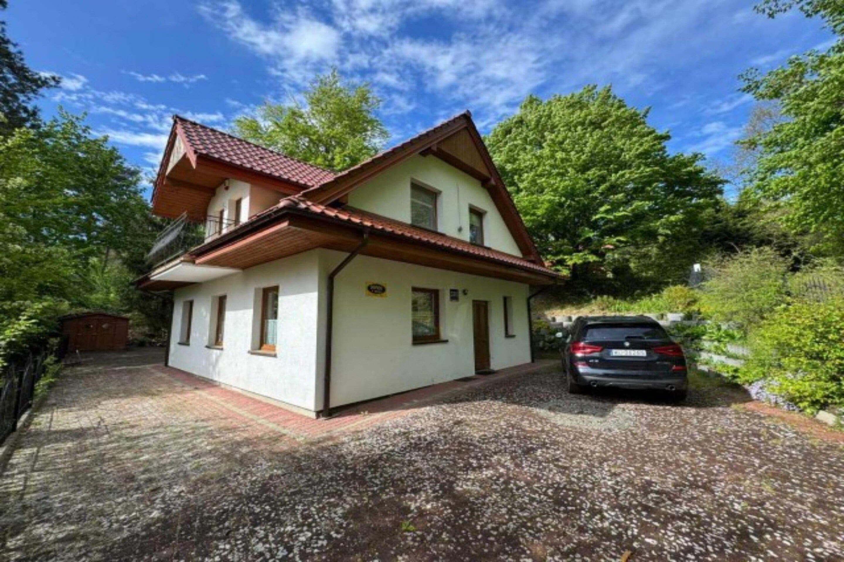 A two-story house with a sloped roof, a gravel driveway, and a parked car.