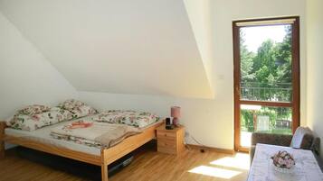 A bedroom with a wooden bed, a nightstand, a lamp, a window with a view of greenery, and a table with a vase of flowers.