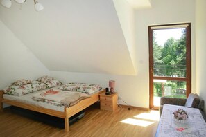 A bedroom with a wooden bed, a nightstand, a lamp, a window with a view of greenery, and a table with a vase of flowers. - Holiday Home in Kretowiny Near Lake (Morag)