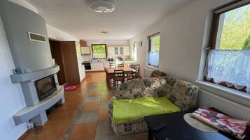 A living room with a sofa, a table, and a fireplace. There is a kitchen in the background.