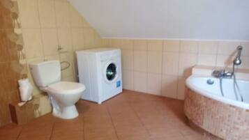 A bathroom with a toilet, washing machine, and bathtub.