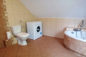 A bathroom with a toilet, washing machine, and bathtub. - Holiday Home in Kretowiny Near Lake (Morag)