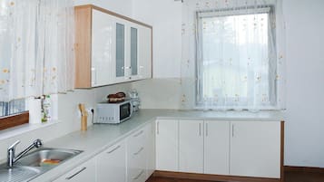 A kitchen with white cabinets, a stainless steel sink, a microwave, and a window with floral curtains.
