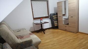 A small room with a wooden floor, a sofa, a radiator, a window with a patterned blind, and a mirror on the wall.