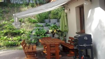 Un patio con una mesa y bancos de madera, una parrilla y una pérgola que ofrece sombra.