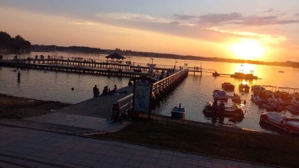 A sunset view of a waterfront area with a pier, boats, and people. - Holiday Home in Kretowiny Near Lake (Morag)