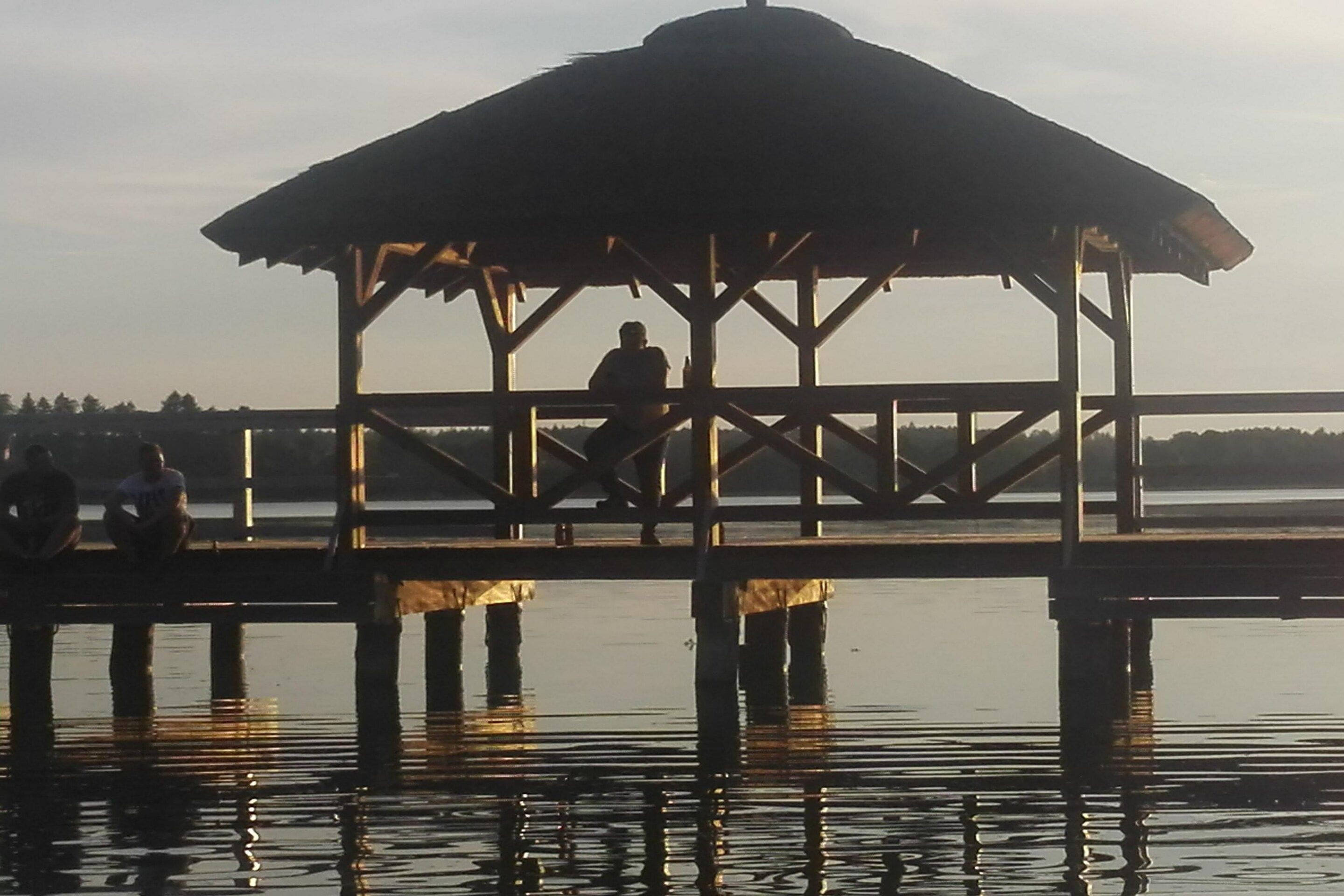A wooden pier with a gazebo structure, extending over calm water.