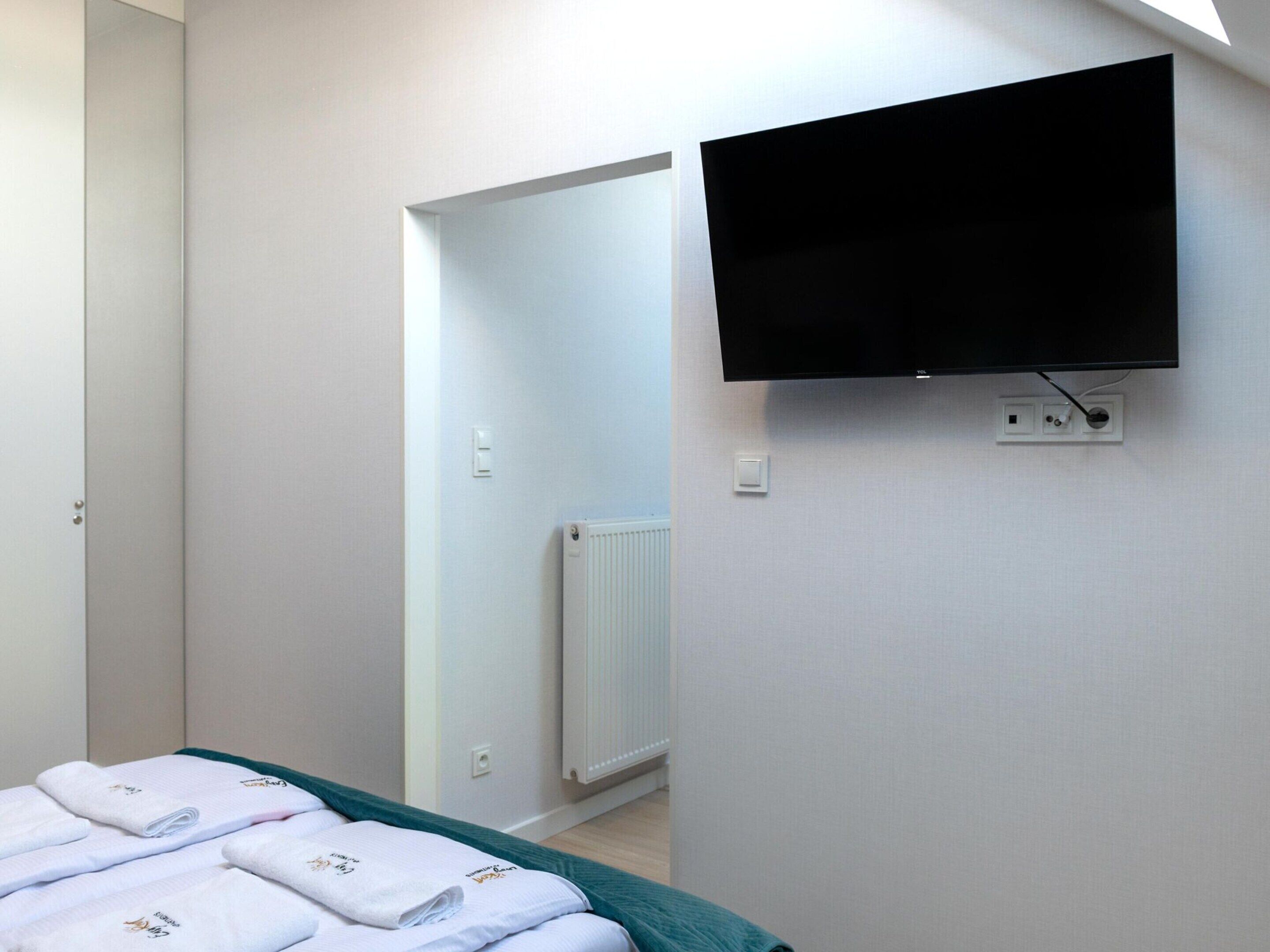 A bedroom with a bed, a TV mounted on the wall, and a radiator.
