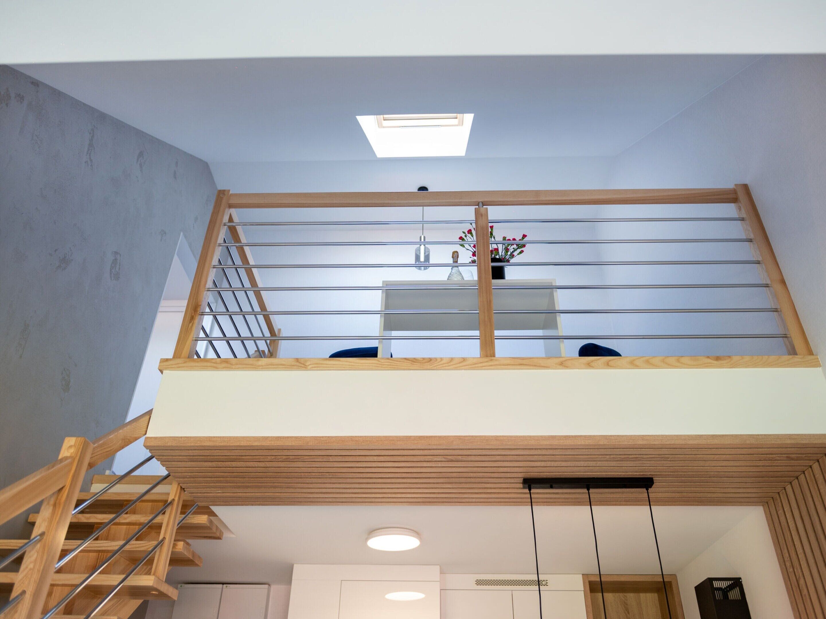 Un interior moderno con una escalera de madera, un entresuelo con barandilla y un tragaluz.