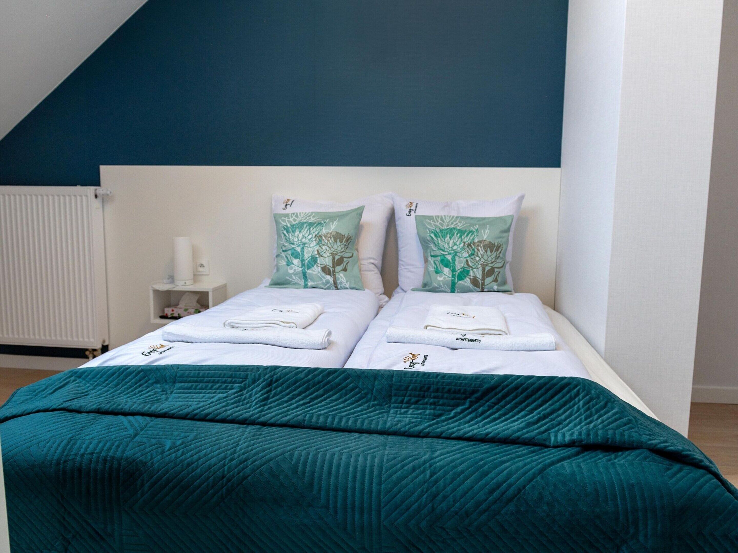 Un lit double avec deux oreillers, une couvre-lit de couleur turquoise et une table de chevet blanche avec une lampe.