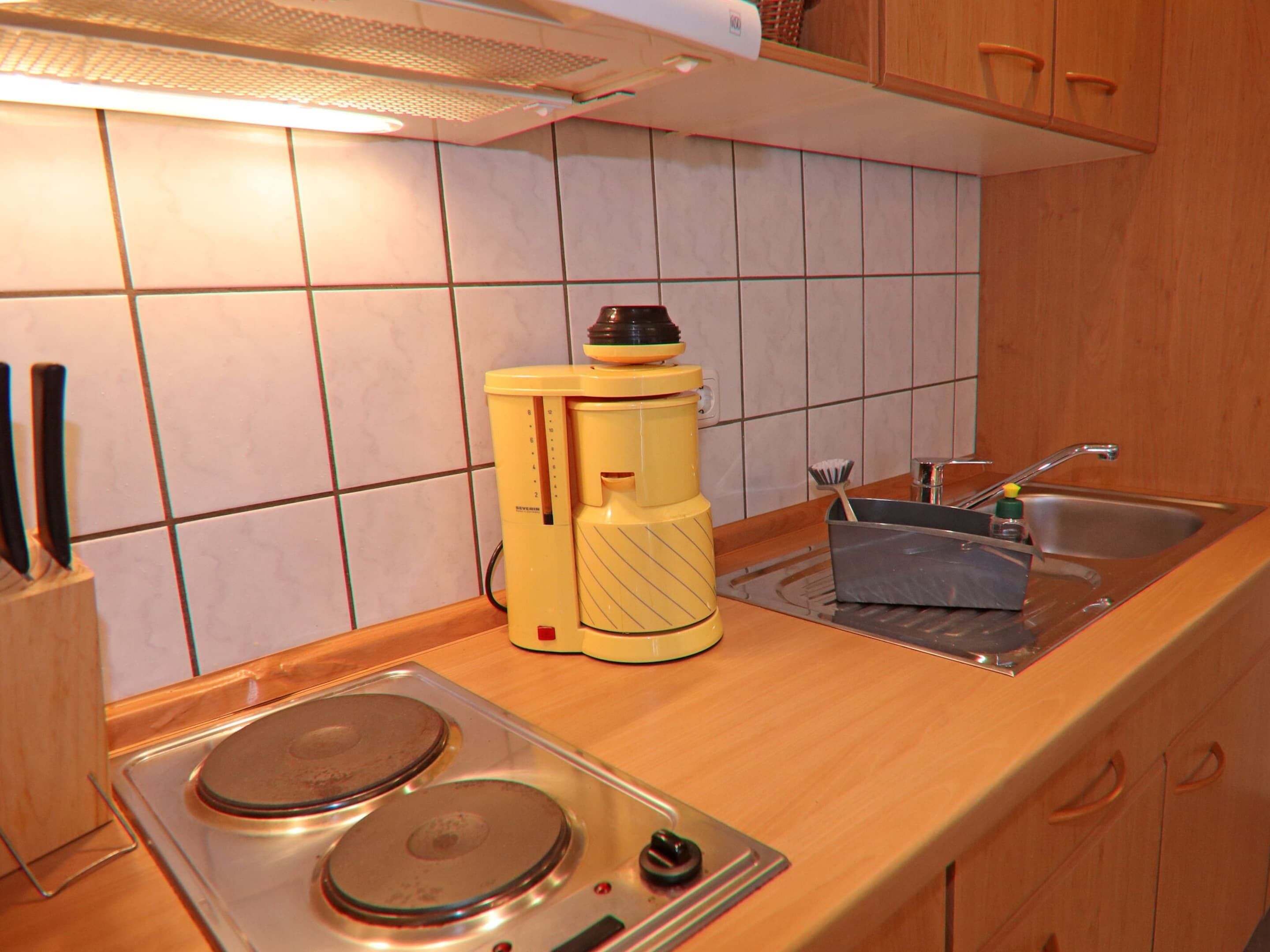 A kitchen with a stove, sink, and a yellow appliance on the counter.