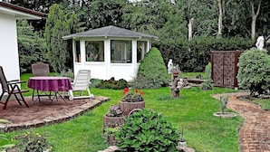 A garden with a gazebo, a brick pathway, and a patio with a table and chairs. - Ferienhauser am Teich, Zinnowitz (Zinnowitz)