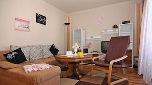 A living room with a sofa, a wooden coffee table, a chair, and a television. - Ferienhauser am Teich, Zinnowitz (Zinnowitz)