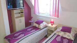 A bedroom with two beds, a TV, a small table with a pink lamp, and a window with pink curtains. - Holiday Home in Dziwnowek by Baltic Beach (Dziwnów)
