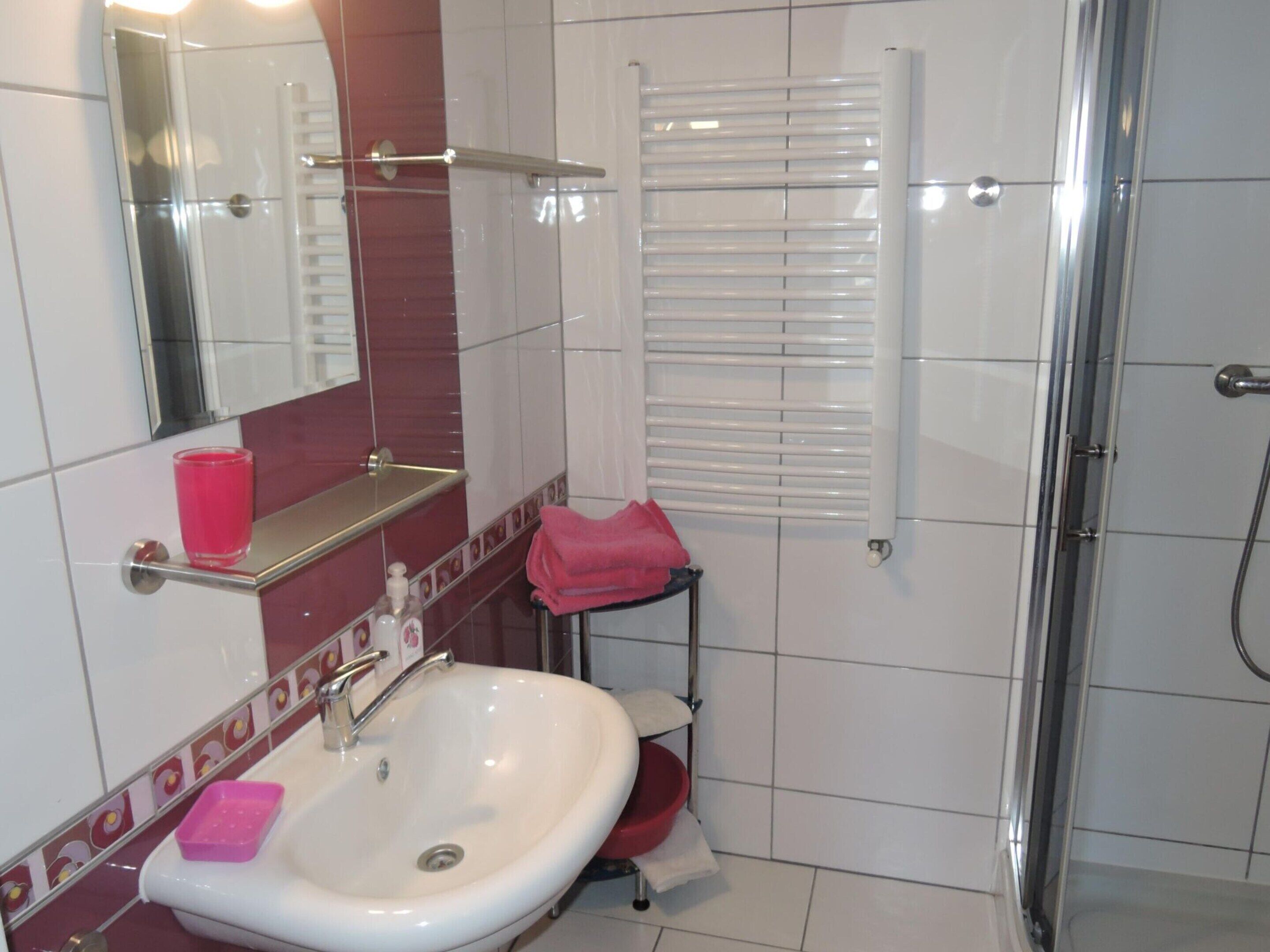 A bathroom with a white sink, a mirror, a red towel, and a shower area.