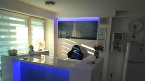 A modern kitchen with a blue-lit island, a sailboat painting on the wall, and a refrigerator. - Holiday Home in Dziwnowek by Baltic Beach (Dziwnów)
