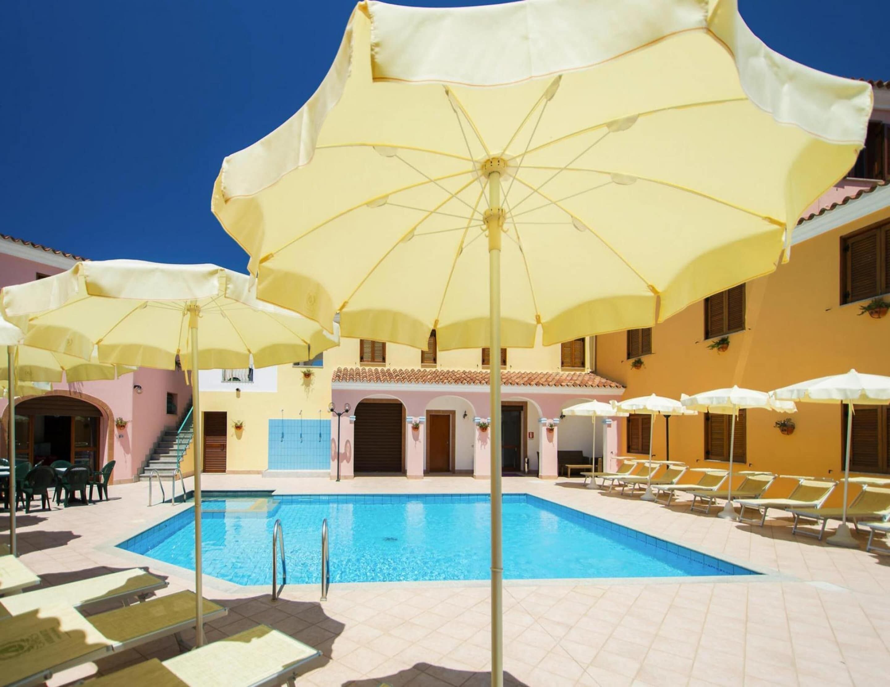 Uma área de piscina com vários guarda-sóis amarelos, espreguiçadeiras e uma piscina azul cristalina.