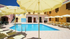 Uma área de piscina com vários guarda-sóis amarelos, espreguiçadeiras e uma piscina azul cristalina.