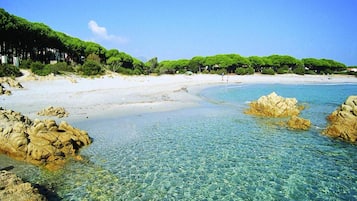 Uma praia com águas cristalinas e rasas, formações rochosas e uma faixa de areia.