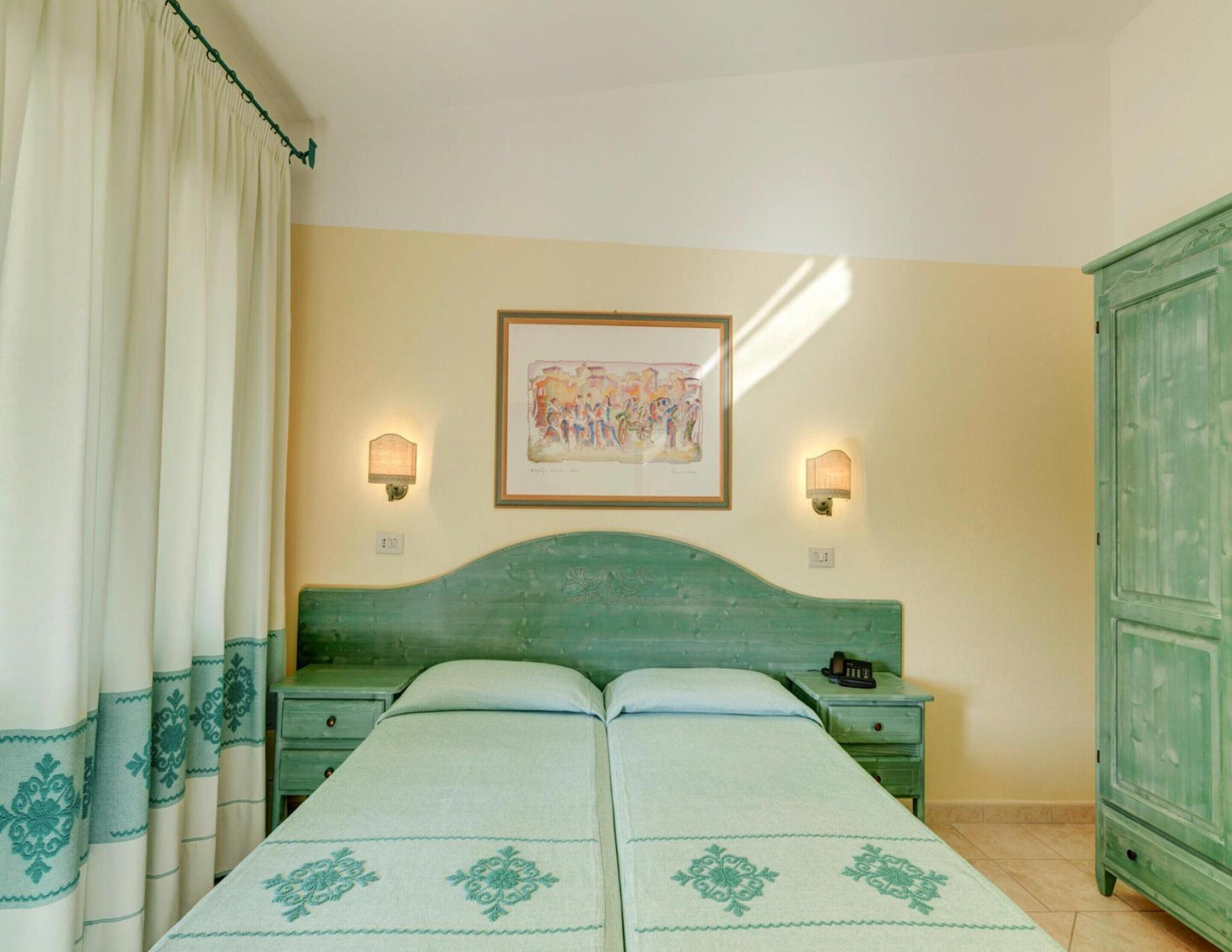 Une chambre avec un lit, deux tables de chevet, une armoire verte et deux lampes fixées au mur.