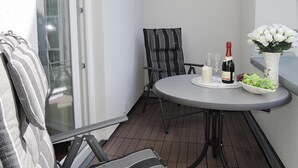 A small outdoor patio with a round table, two chairs, a bottle of wine, glasses, a candle, and a bowl of grapes. - Apartment in Eifel With Terrace and Nature (Lissendorf)