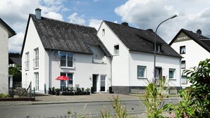 A white building with a black roof, a red umbrella, and a sign that says "HOTEL". - Apartment in Eifel With Terrace and Nature (Lissendorf)