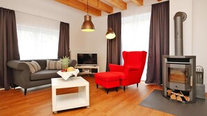 A modern living room with a sofa, a red armchair, a white coffee table, a TV, and a wood-burning stove. - Apartment in Eifel With Terrace and Nature (Lissendorf)
