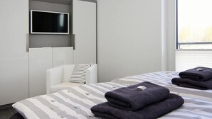 A modern hotel room with a bed, a TV mounted on a wall, and a window providing a view. - Modern Eingerichtetes Ferienhaus auf Usedom (Peenemünde)